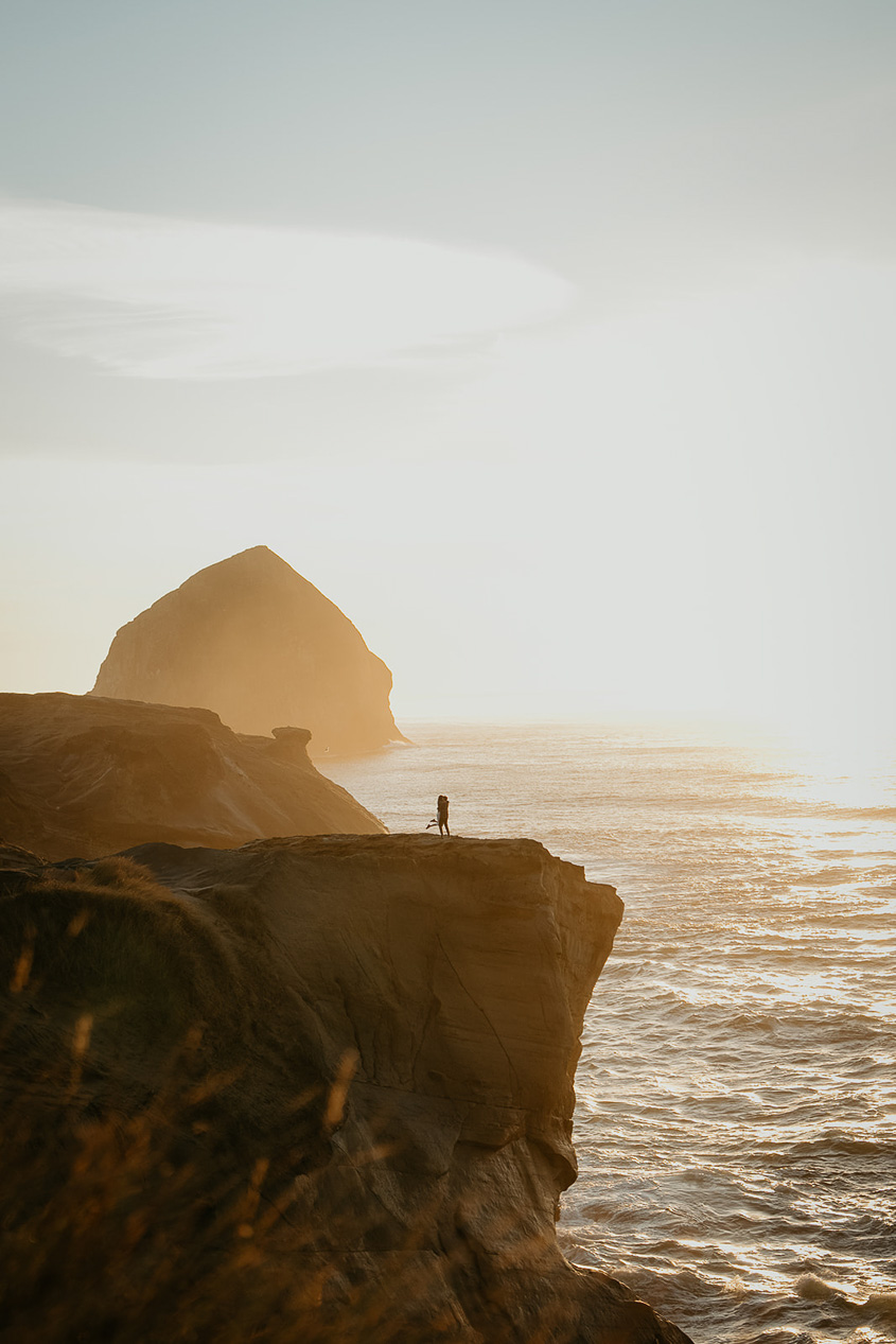 a couple dancing on a cliffside at sunset, with the Oregon ocean and a sea stack in the background during their Cape Kiwanda Engagement.