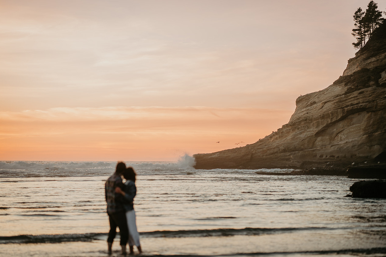 a couple hugging each other watching the sun set over the ocean during their Cape Kiwanda Engagement.