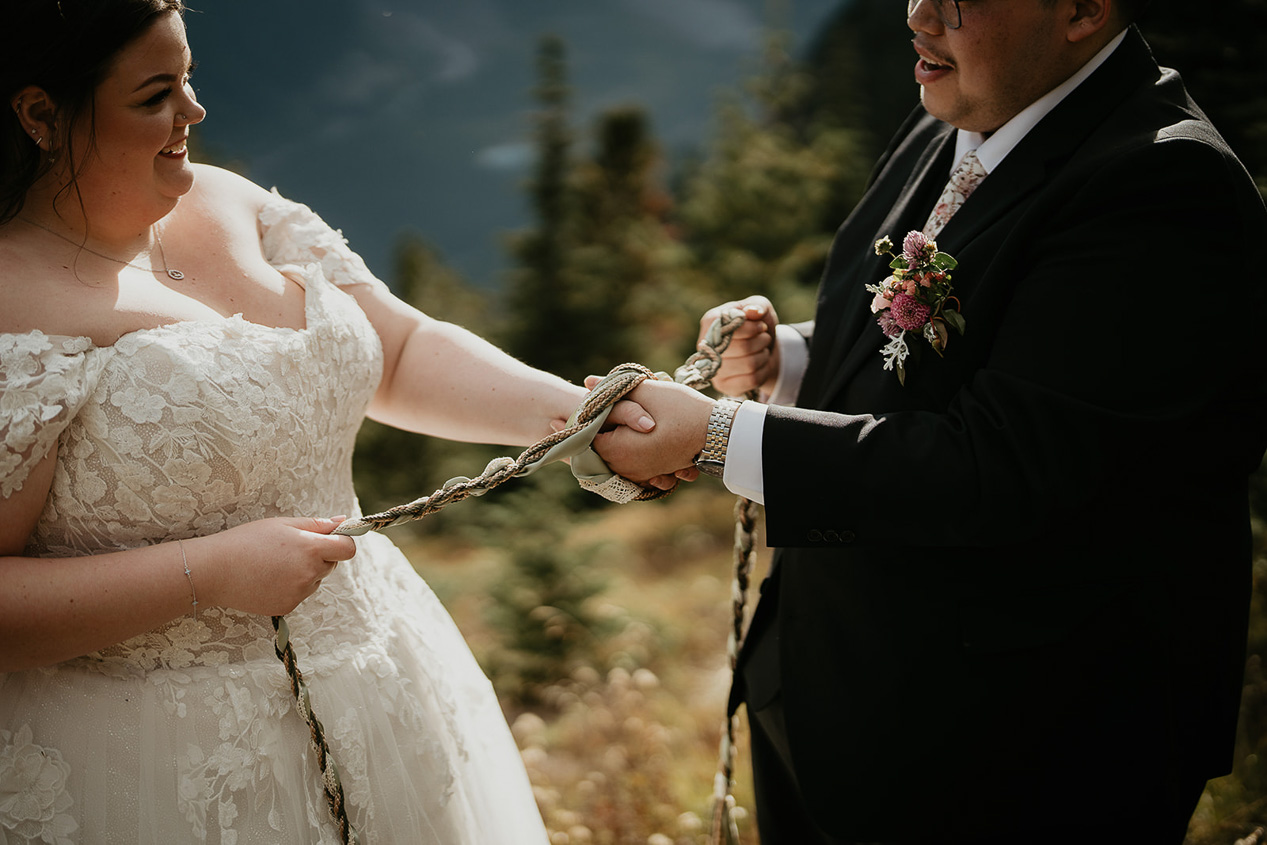 a couple performing a hand fasting ceremony, part of what an elopement ceremony can look like.