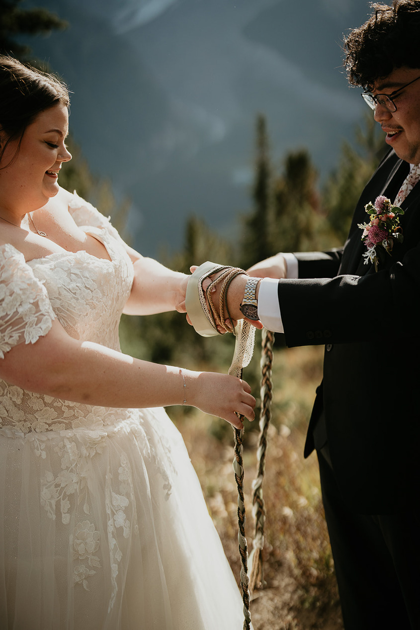 a couple performing a hand fasting ceremony, part of what an elopement ceremony can look like.