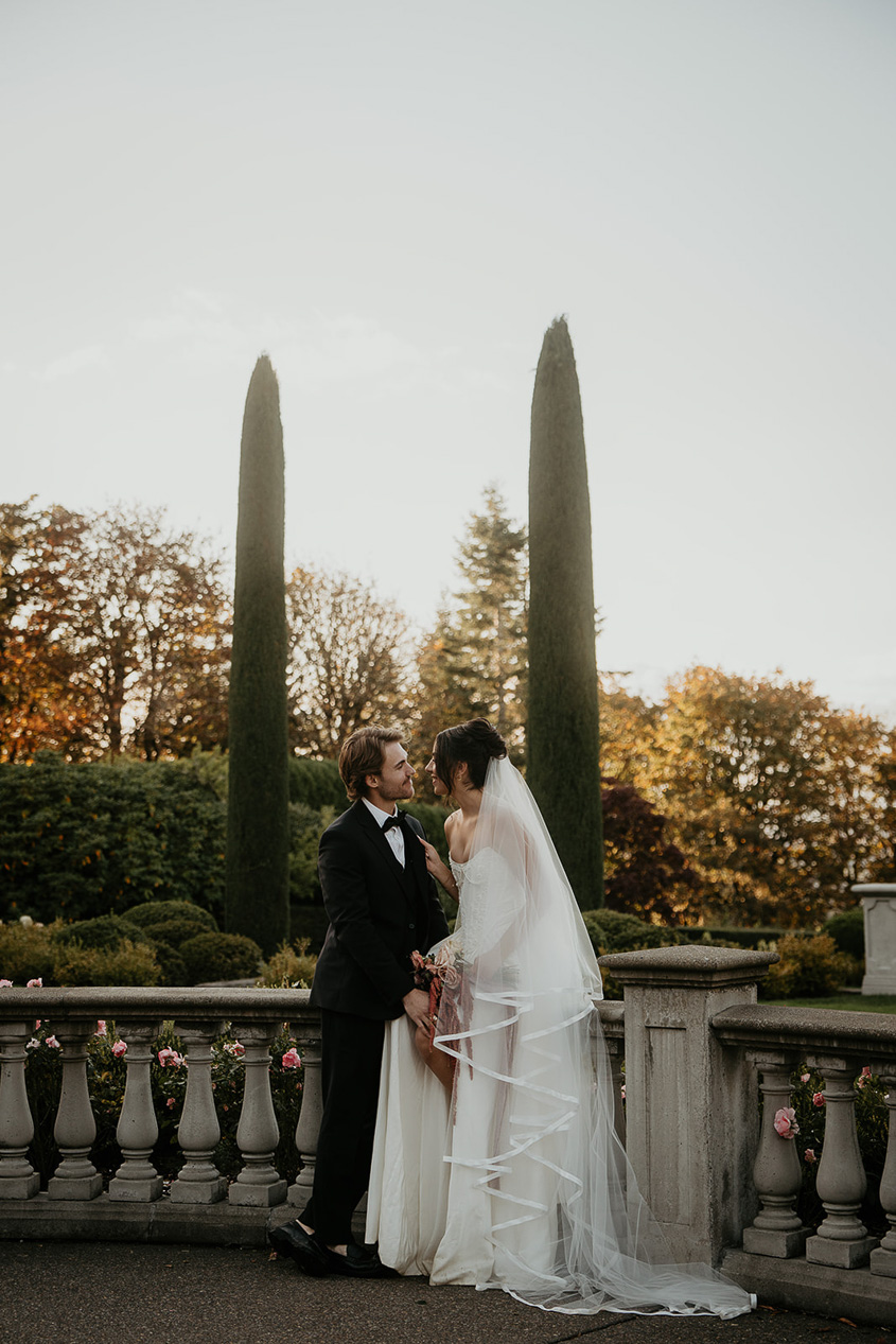 newlyweds holding hands with stone architecture and trees in the background.