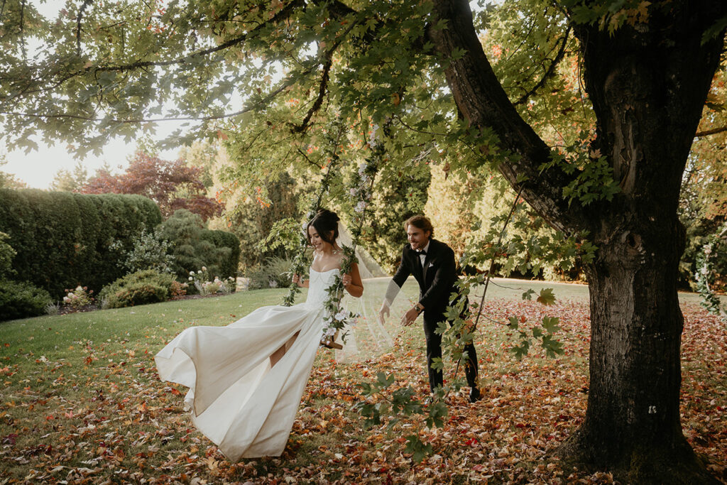 newlyweds swinging on a swing hanging from a large maple tree during their Chateau de Michellia wedding.