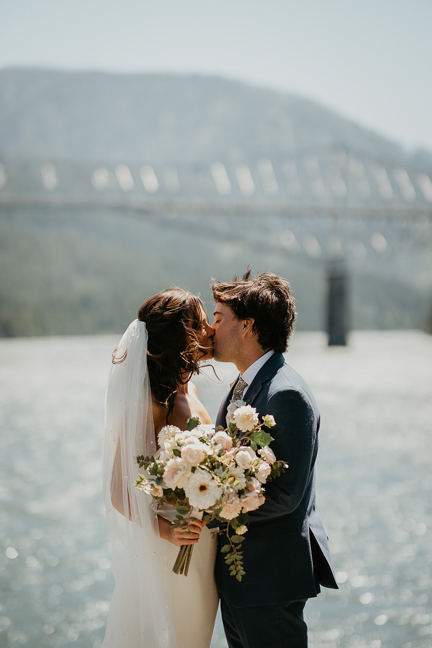a couple kissing with the Bridge of the Gods in the background on Thunder Island, one of the best columbia river gorge wedding venues.