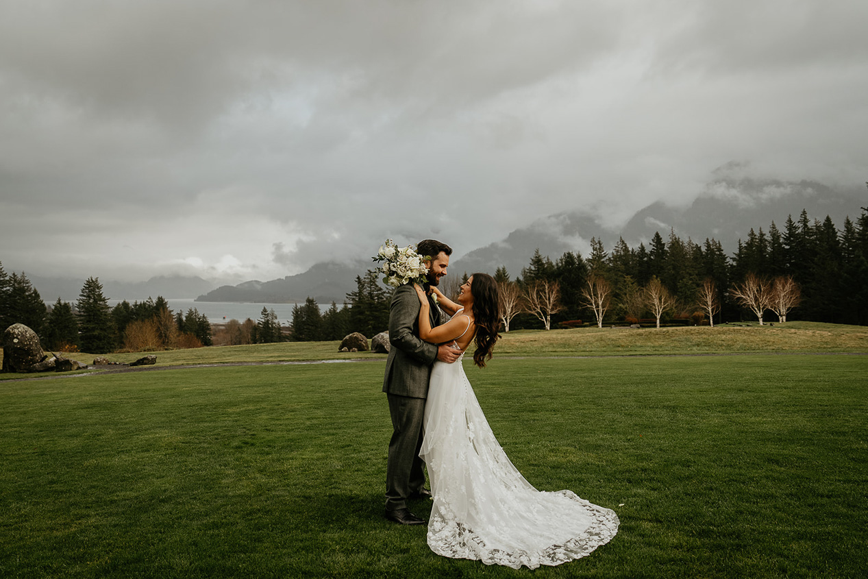a couple hugging withe fields and mountains in the background at skamania lodge, one of the best columbia river gorge wedding venues.
