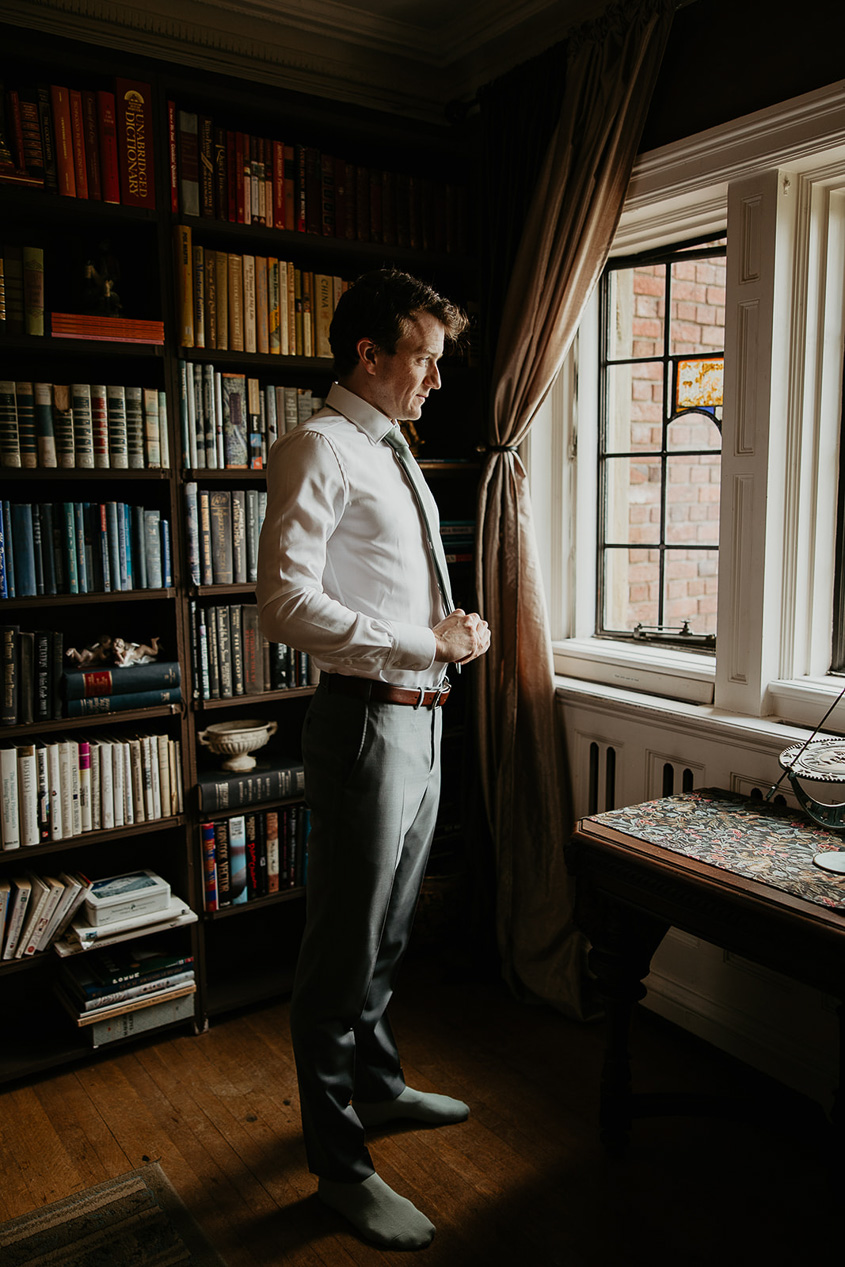the groom adjusting his suit in a study. 