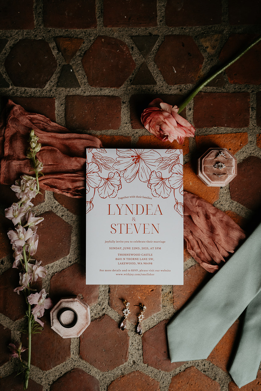 a wedding invite, flowers, a tie, a ring, and other decorations on a brick background.