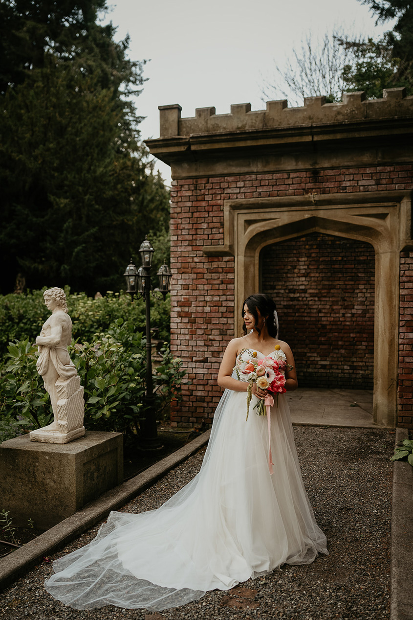 the bride standing in a garden next to a stone statue.