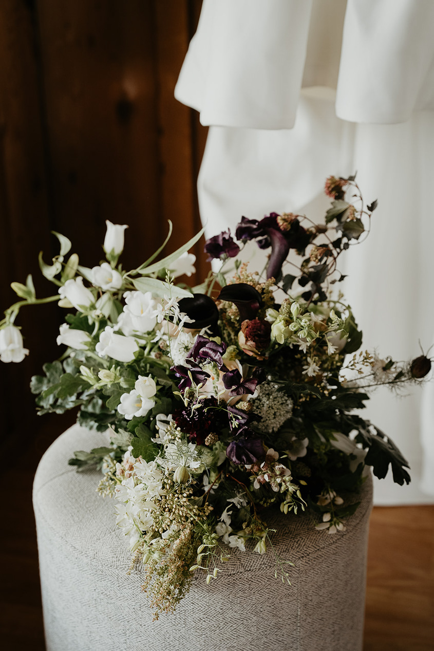 a bouquet of flowers on a white ottoman by a wedding dress.