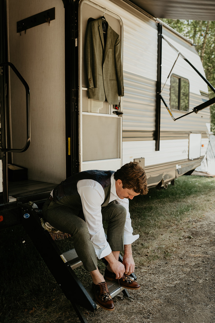 the groom tying his shoes outside his trailer during his rustic barn wedding.