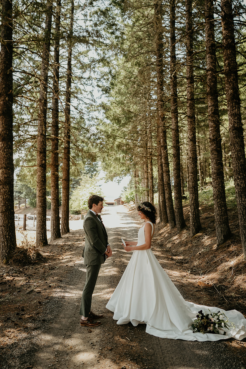 the newlyweds sharing private vows on a dirt road surrounded by trees during their rustic barn wedding.