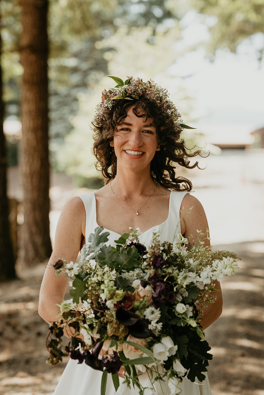 the bride holding a bouquet of flowers and wearing a flower crown during her rustic barn wedding.
