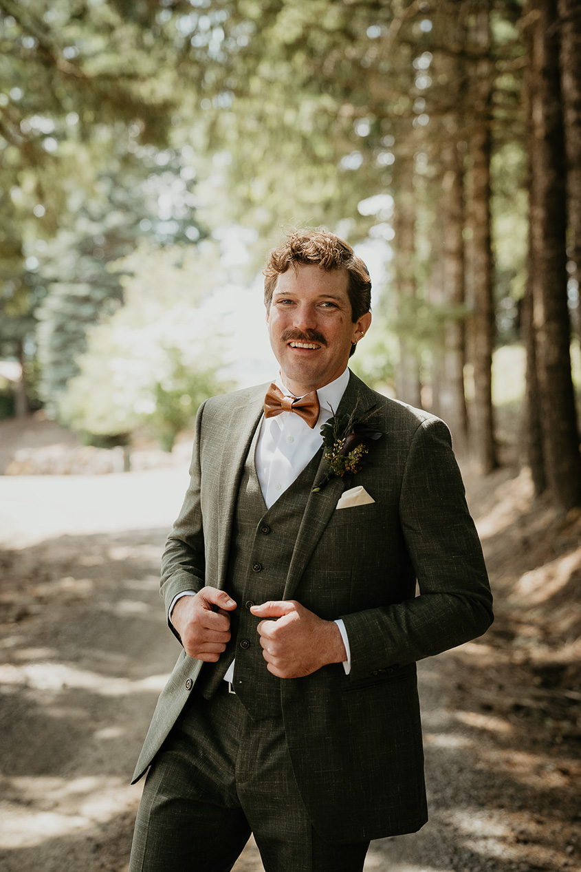 the groom adjusting his jacket and smiling during his rustic barn wedding.