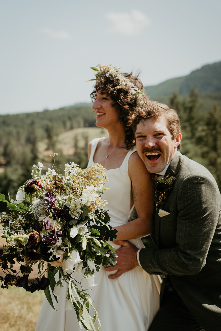 the bride and groom laughing and smiling in a field during their rustic barn wedding.
