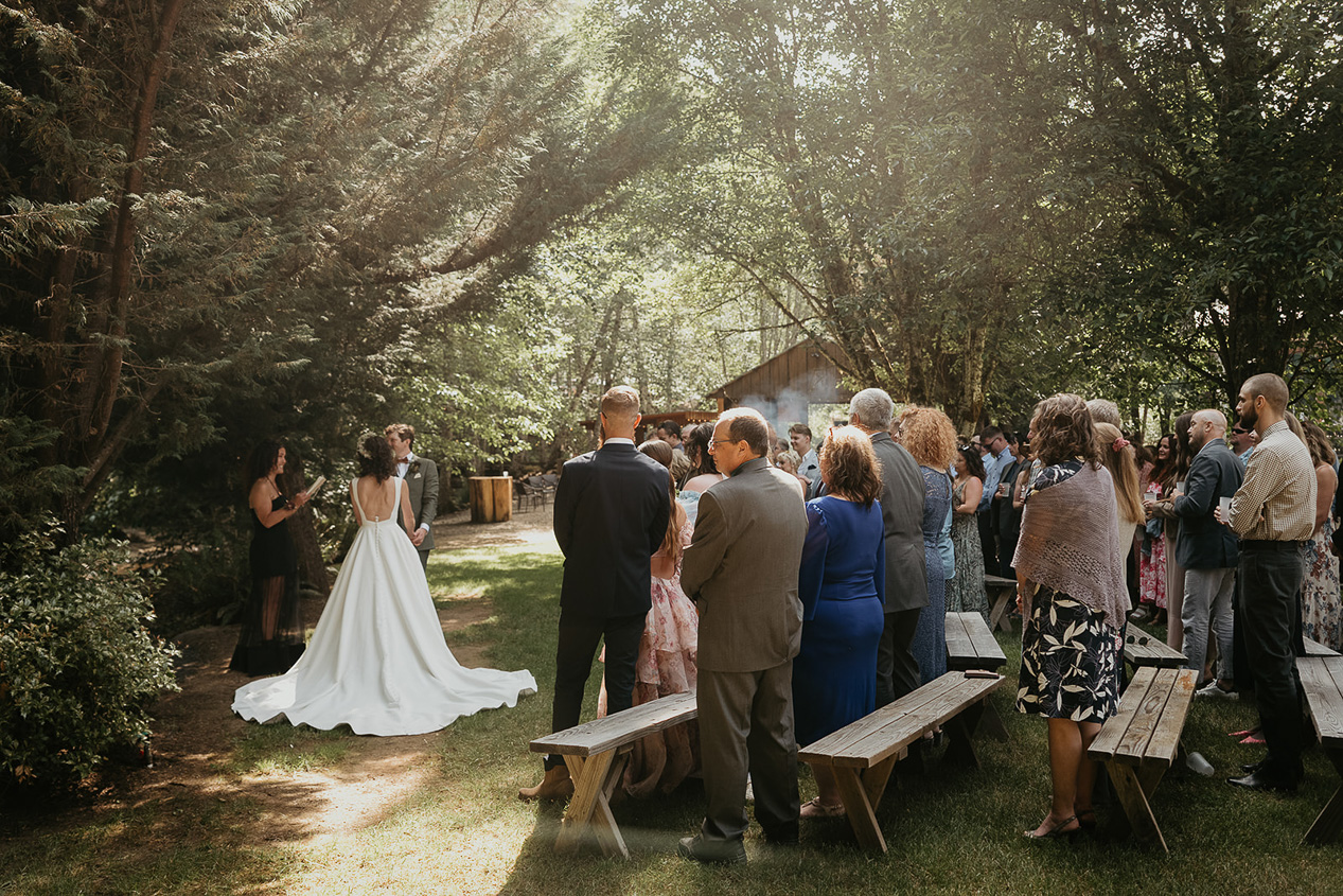 the newlyweds during their ceremony under tree cover, with their guests watching them on during their rustic barn wedding.