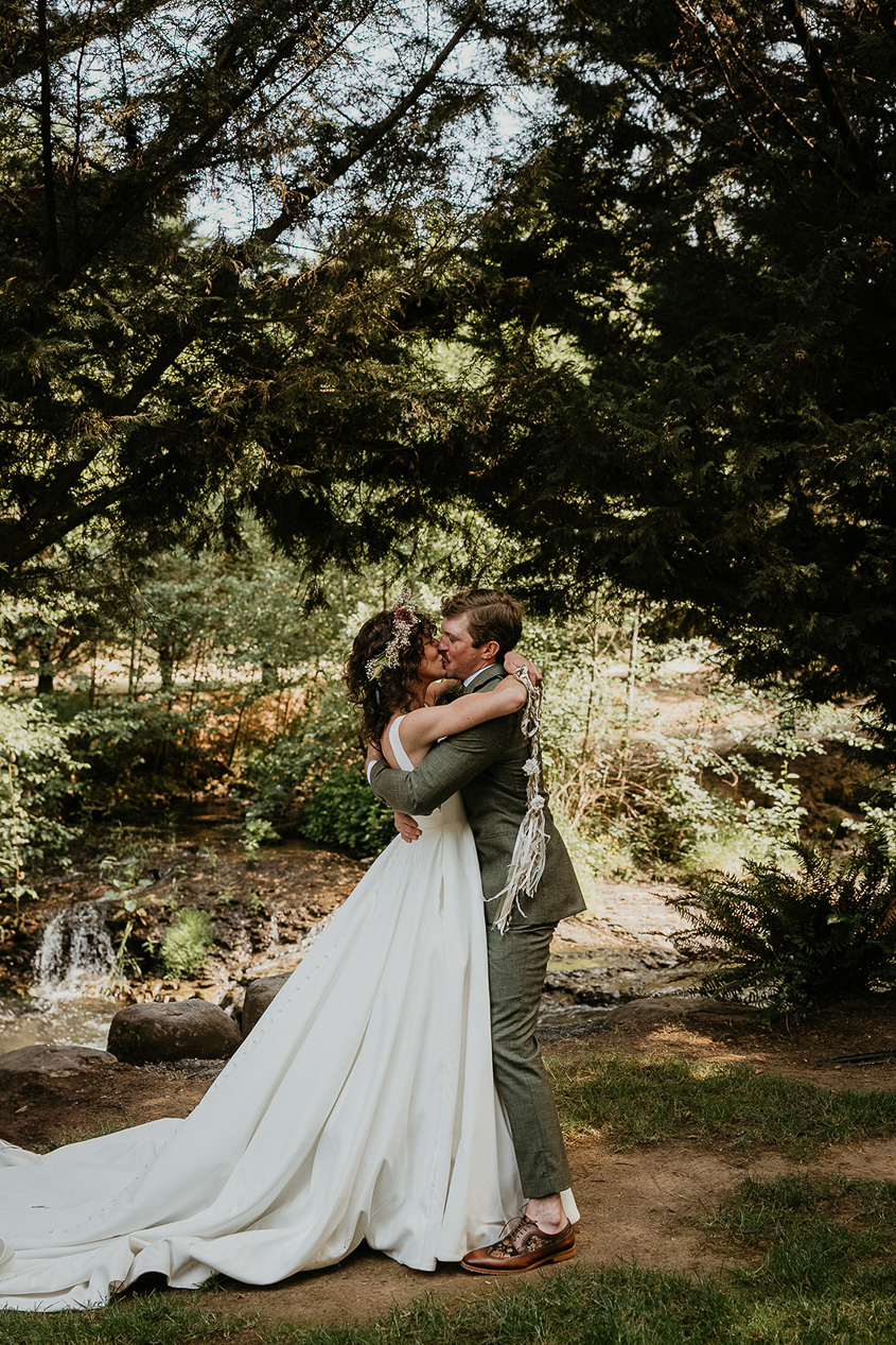 the newlyweds kissing under a tree with a river in the background.