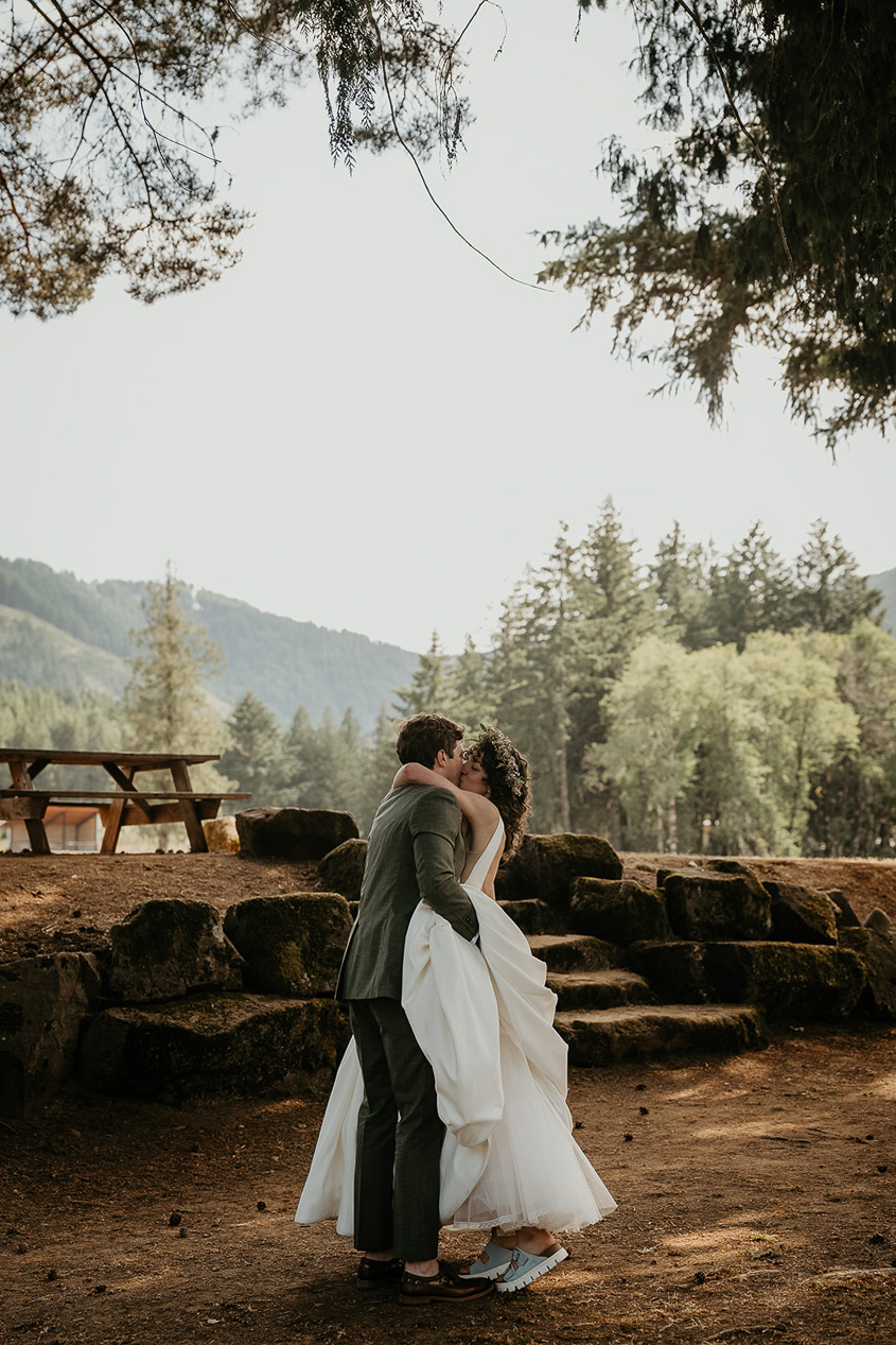 the newlyweds kissing under a tree with forests and mountains in the background.