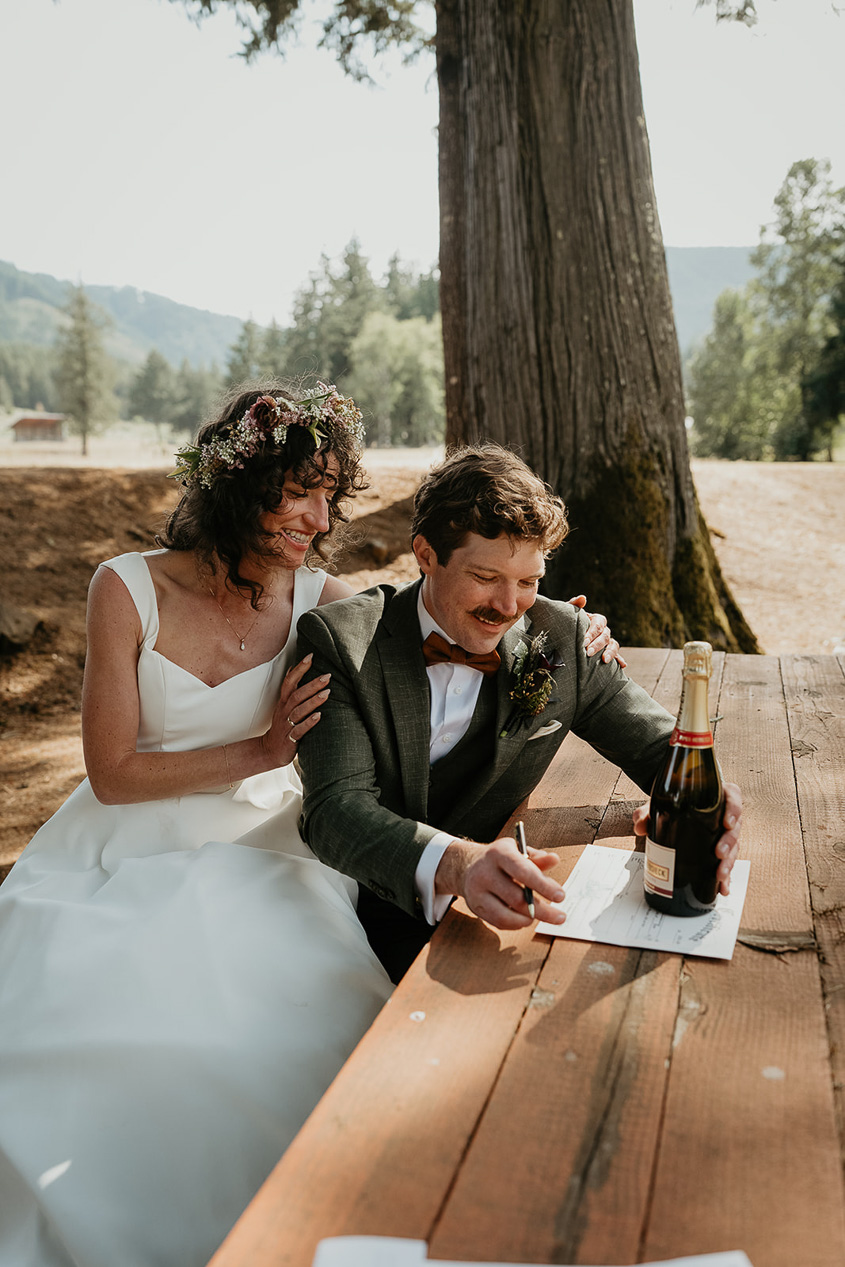 the newlyweds signing their marriage certificate on a picnic bench during their rustic barn wedding.