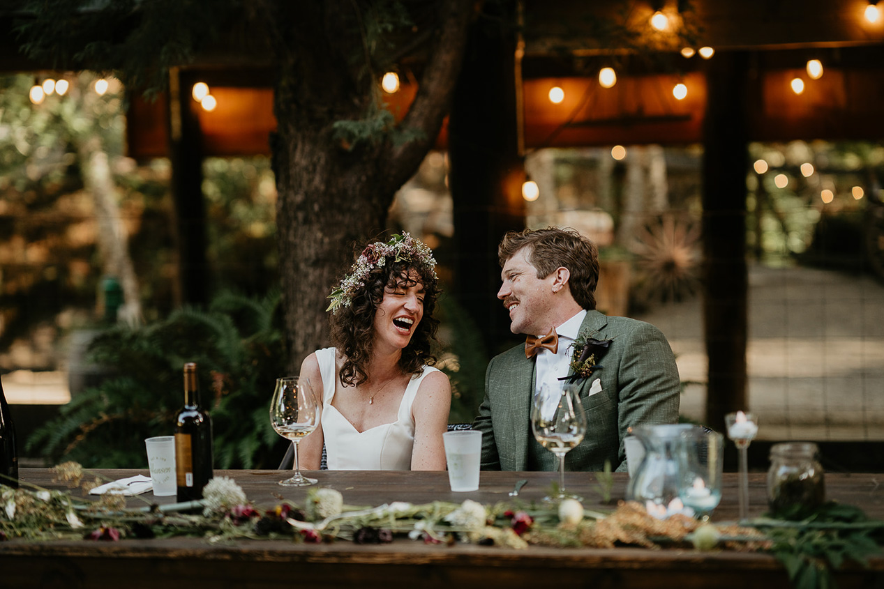 the newlyweds laughing at their dinner table during their rustic barn wedding.