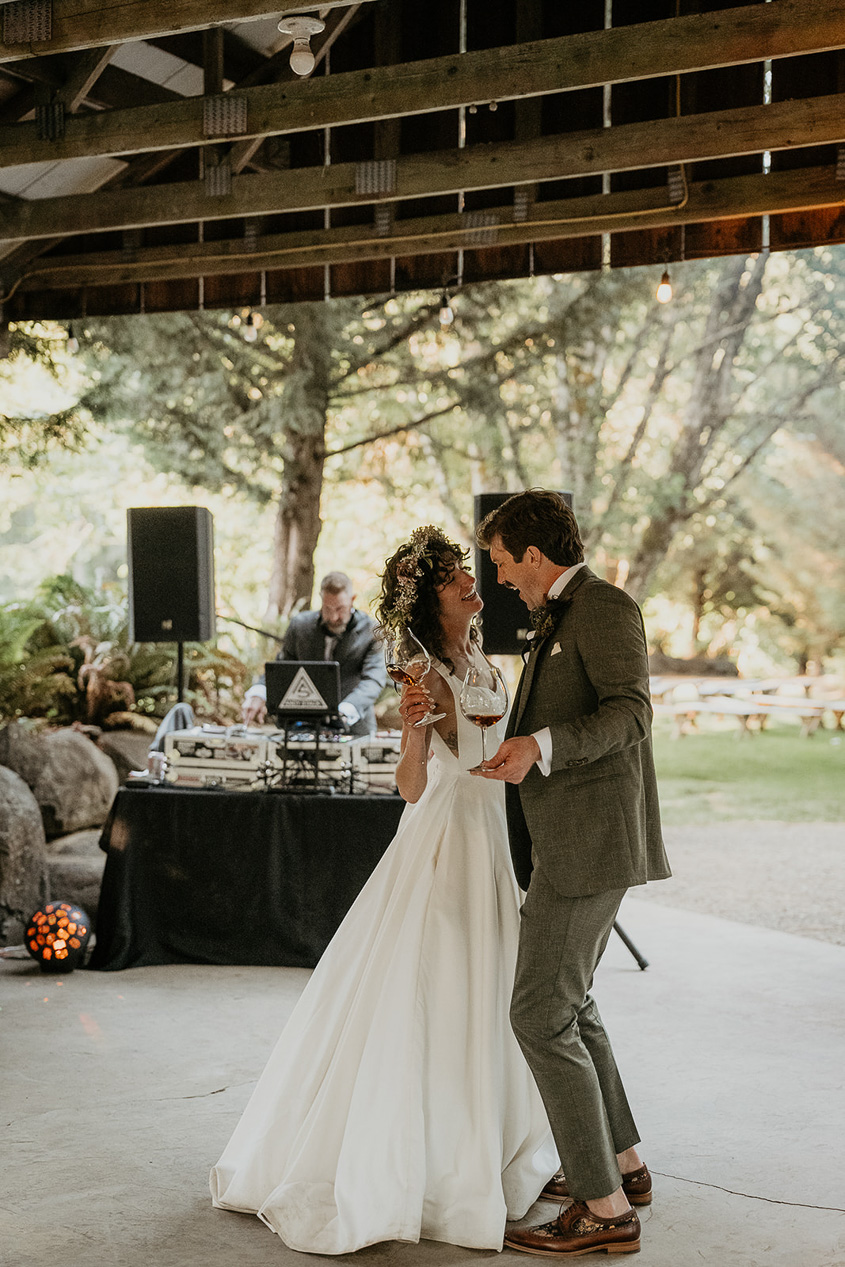 newlyweds holding wine glasses and dancing during their rustic barn wedding.