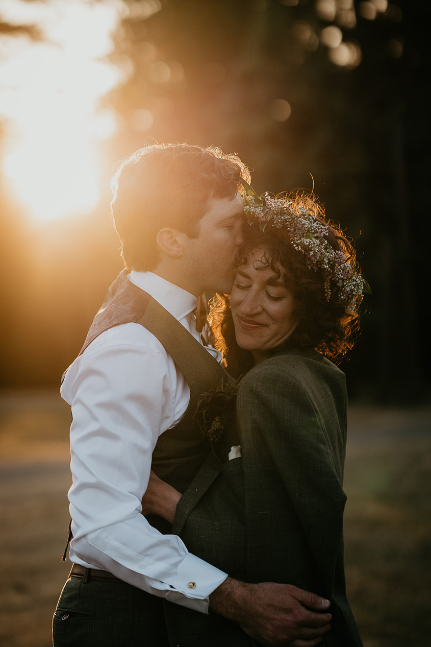 newlyweds hugging and hissing in a grassy field at sunset.