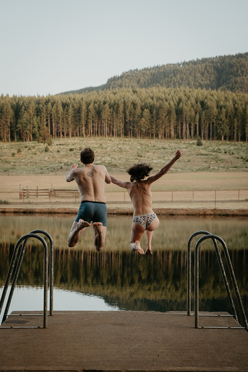 newlyweds jumping in a lake with a forest in the background during their rustic barn wedding.