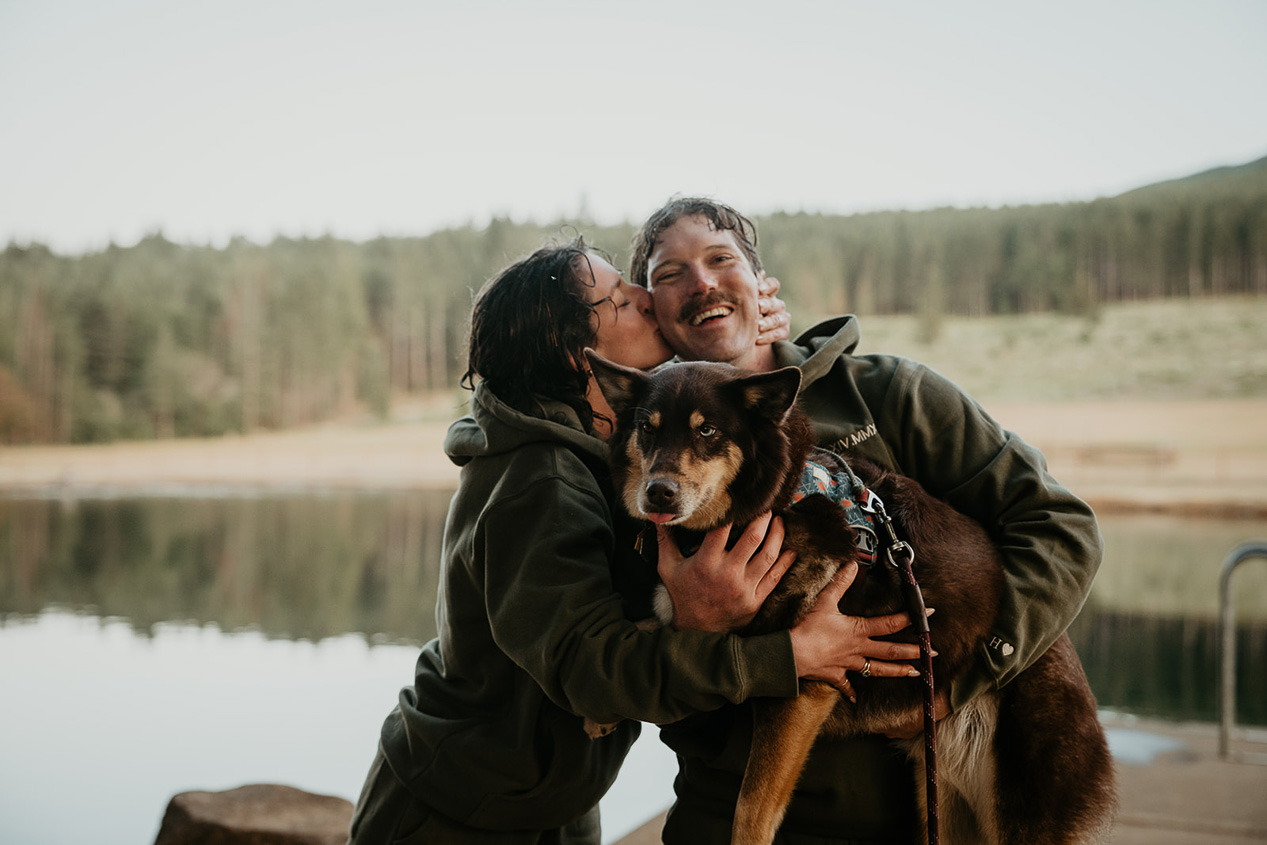 newlyweds smiling and kissing while holding their dog during their rustic barn wedding.