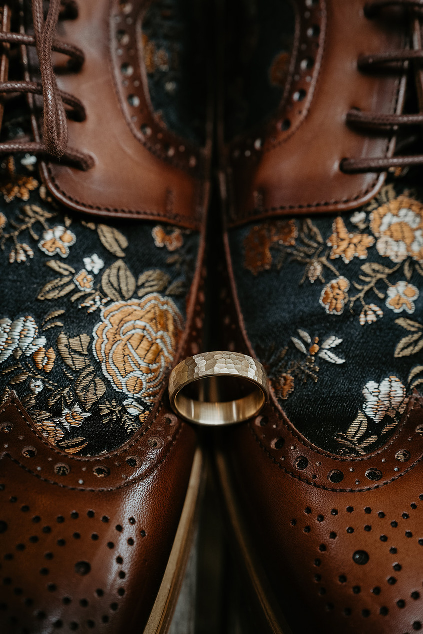 a wedding ring placed between dress shoes.