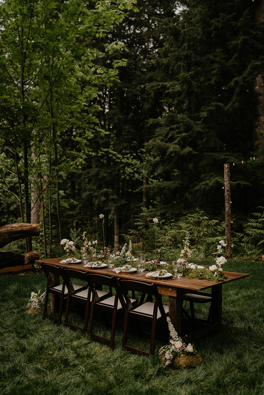 a decorated wedding dinner table on a grassy lawn with forests in the background.