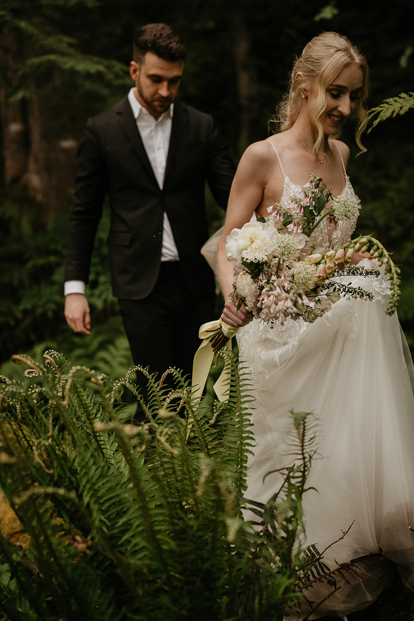 newlyweds walking through fern while exploring the forest.