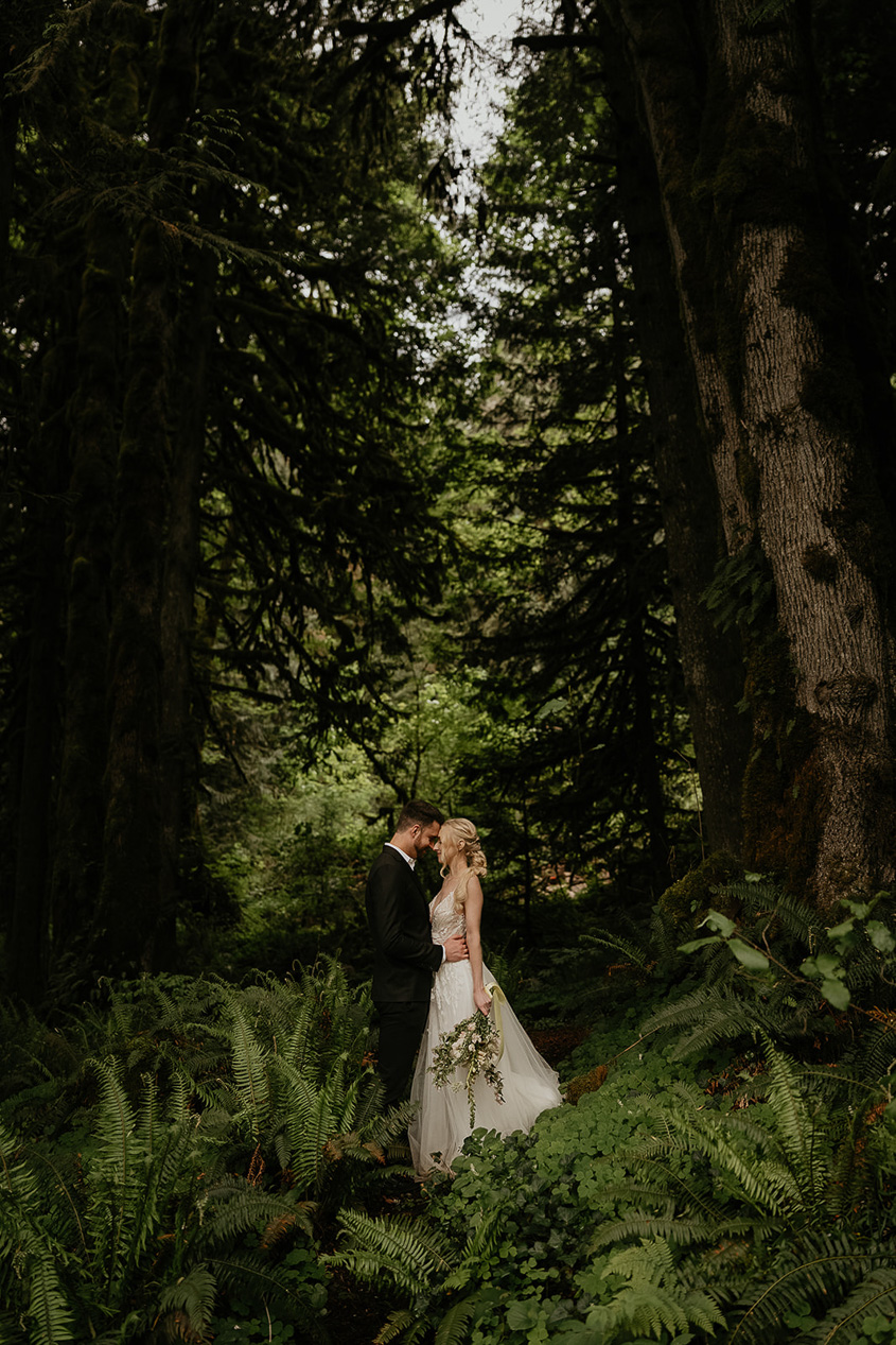 newlyweds embracing each other in the middle of a dense forest.