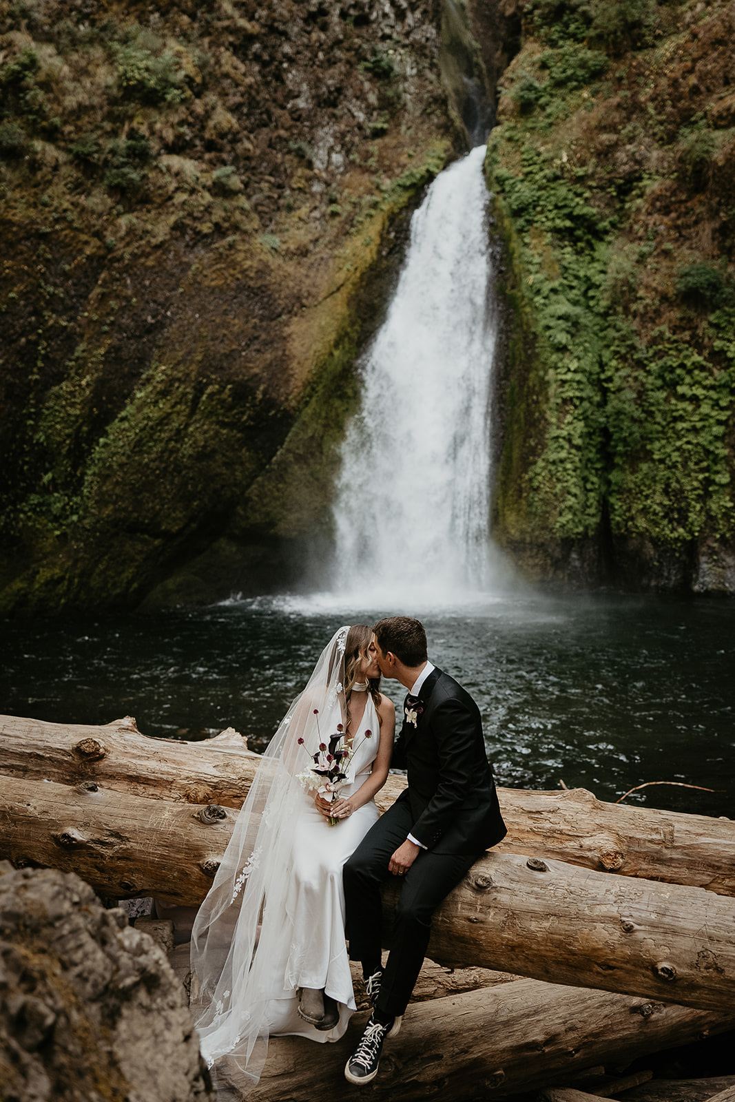 newlyweds sitting in front of a waterfall, which they included as part of their plan for their micro wedding.