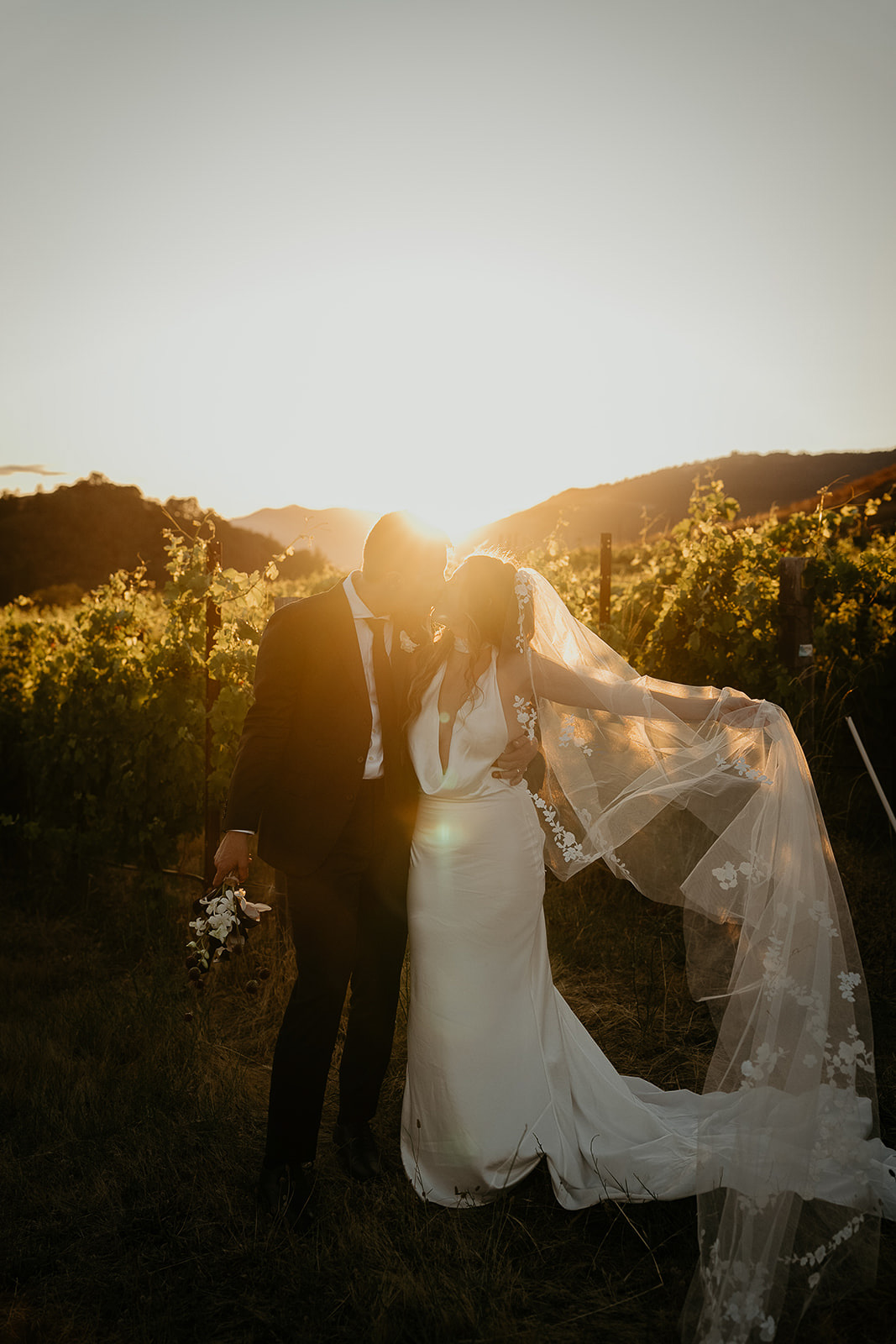 newlyweds kissing at sunset in a vineyard, which they included as part of their plan for their micro wedding.
