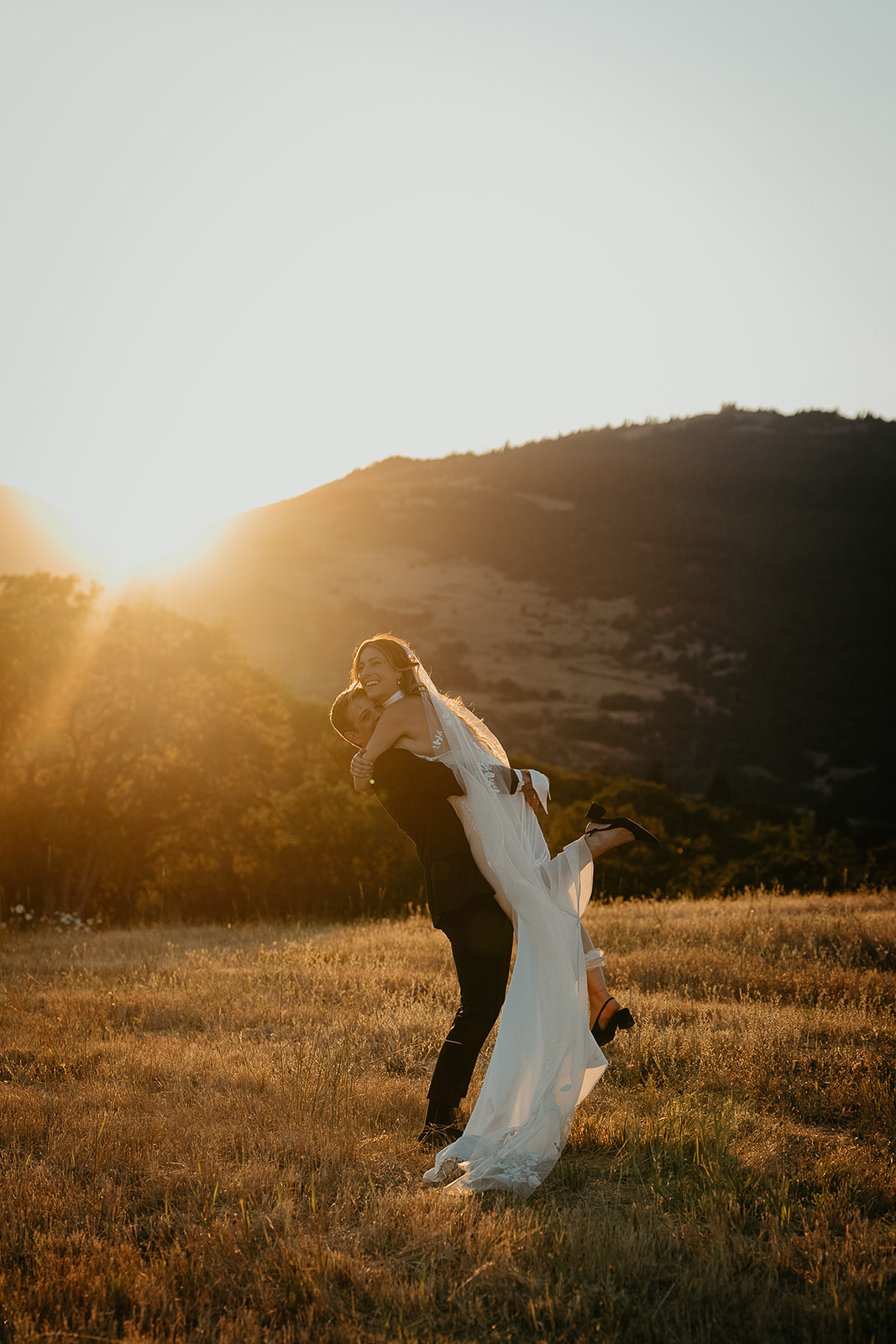 newlyweds hugging at sunset in a field.
