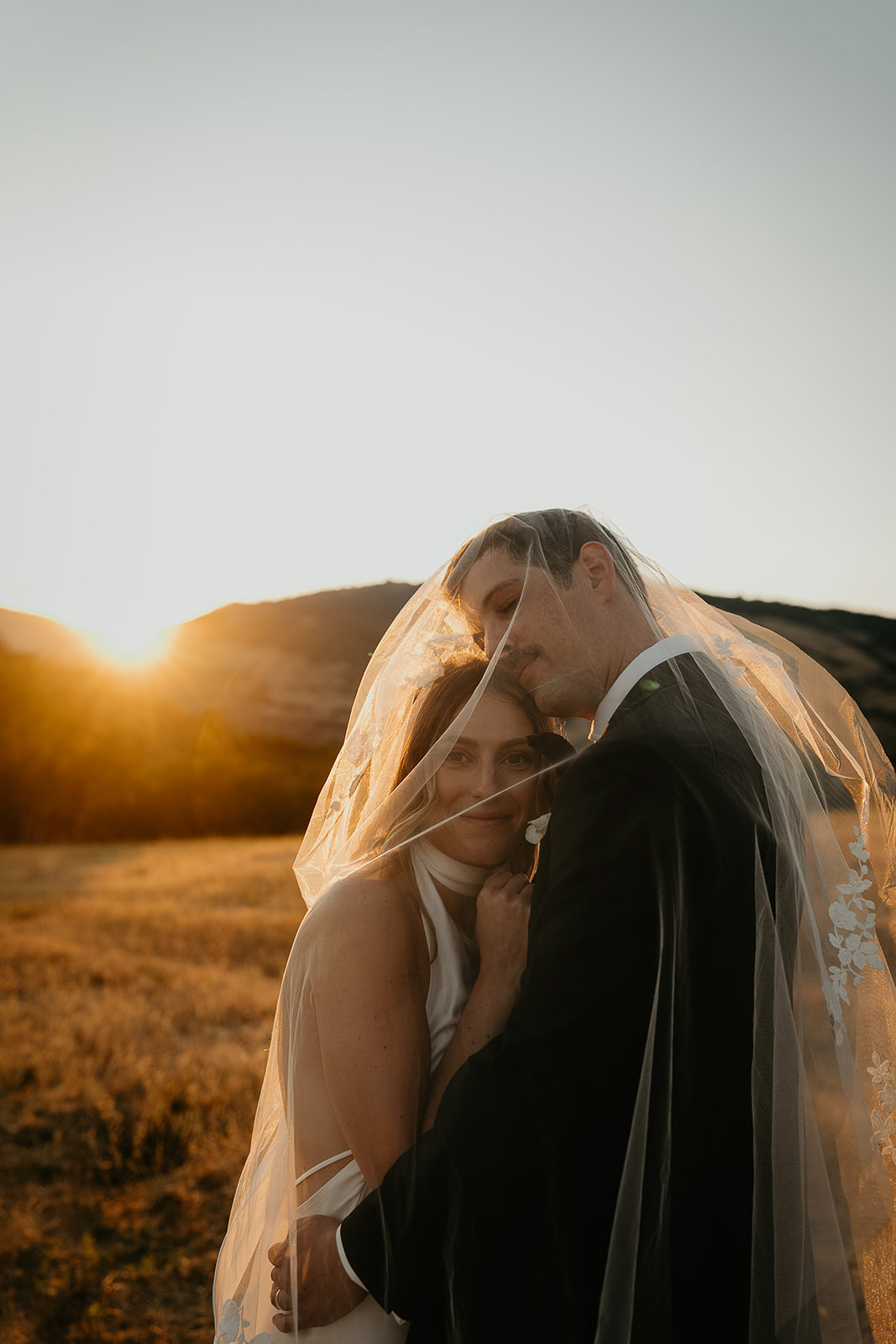 newlyweds hugging at sunset in a field.