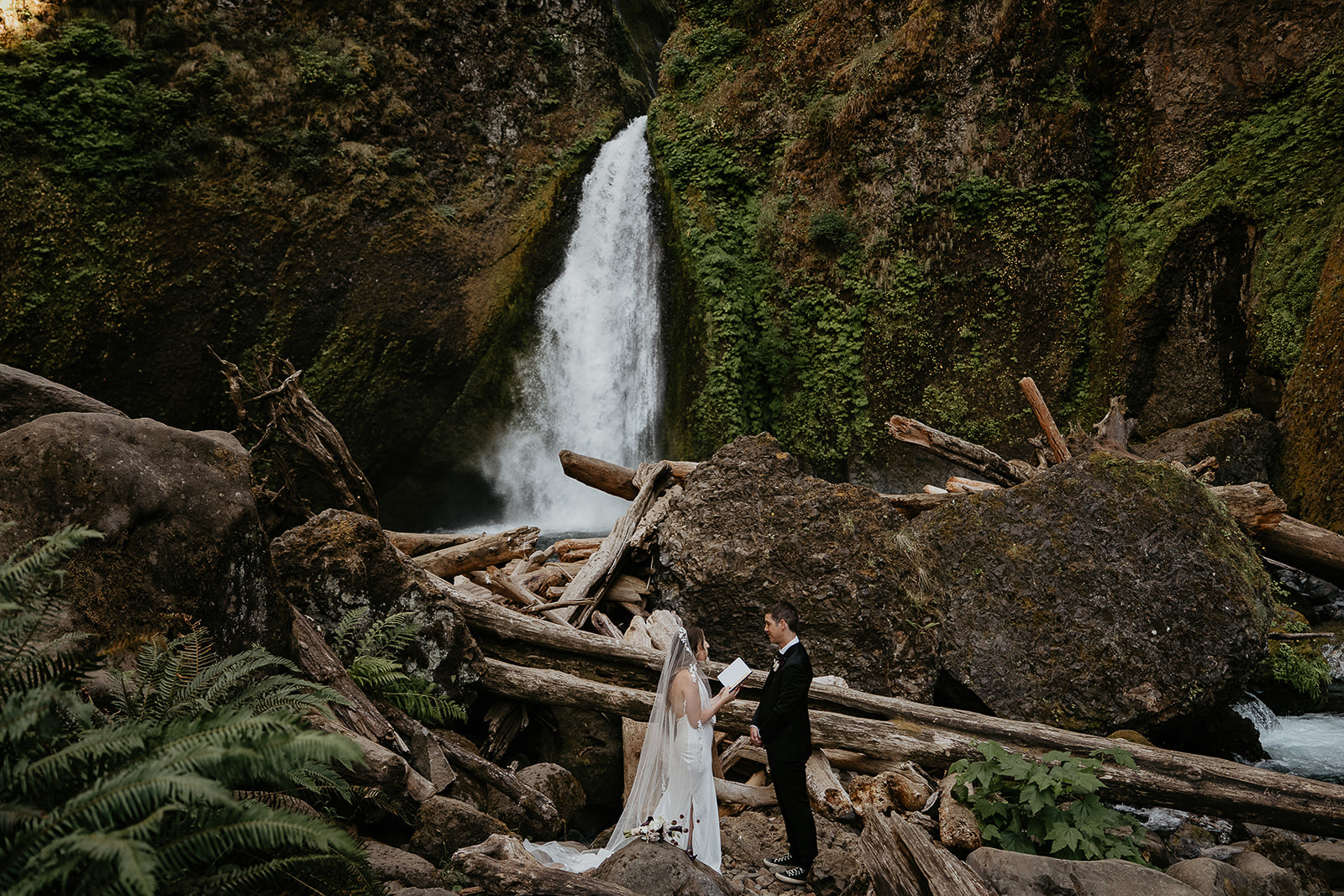 newlyweds exchanging vows in front of a waterfall.