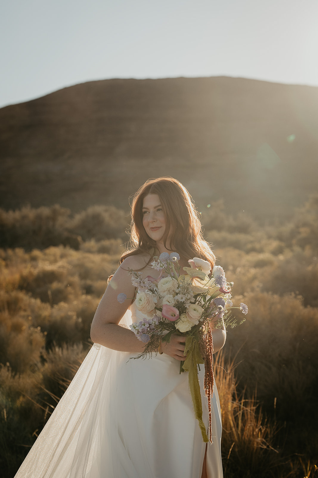 the bride holding her bouquet looking off to the side among desert bushes during their Alvord Desert, Oregon elopement.
