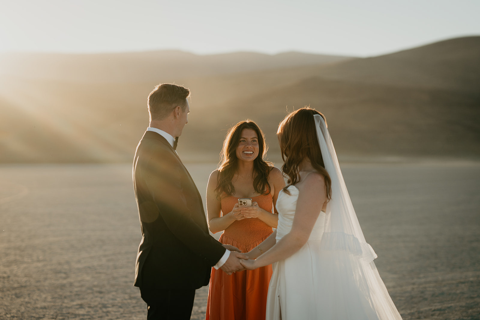 newlyweds holding hands as their officiant shares a message during their Alvord Desert, Oregon elopement.