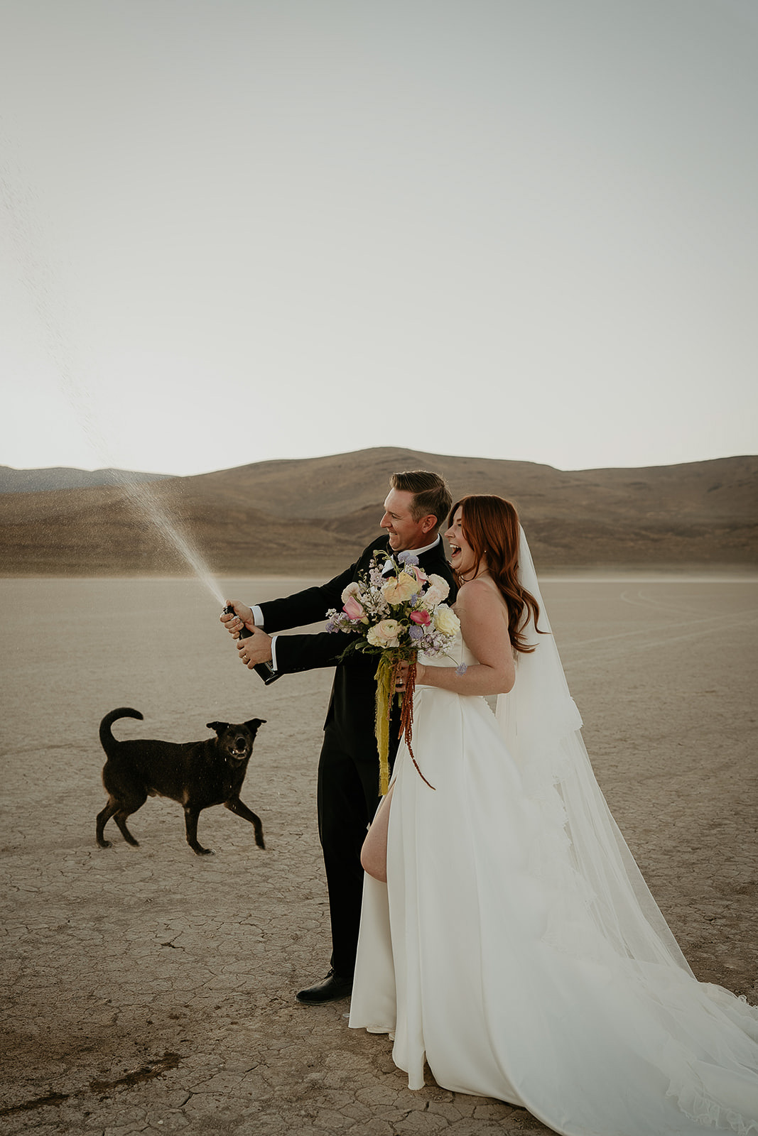 newlyweds spraying a bottle of champagne in the desert during their Alvord Desert, Oregon elopement.