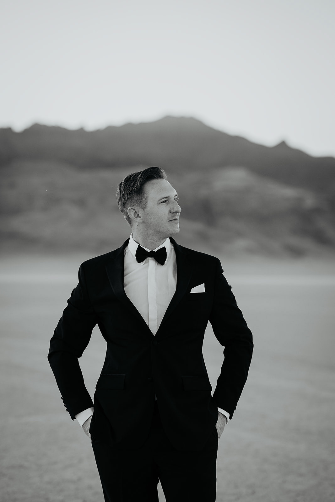 the groom with his hands in his pockets looking off into the distance.