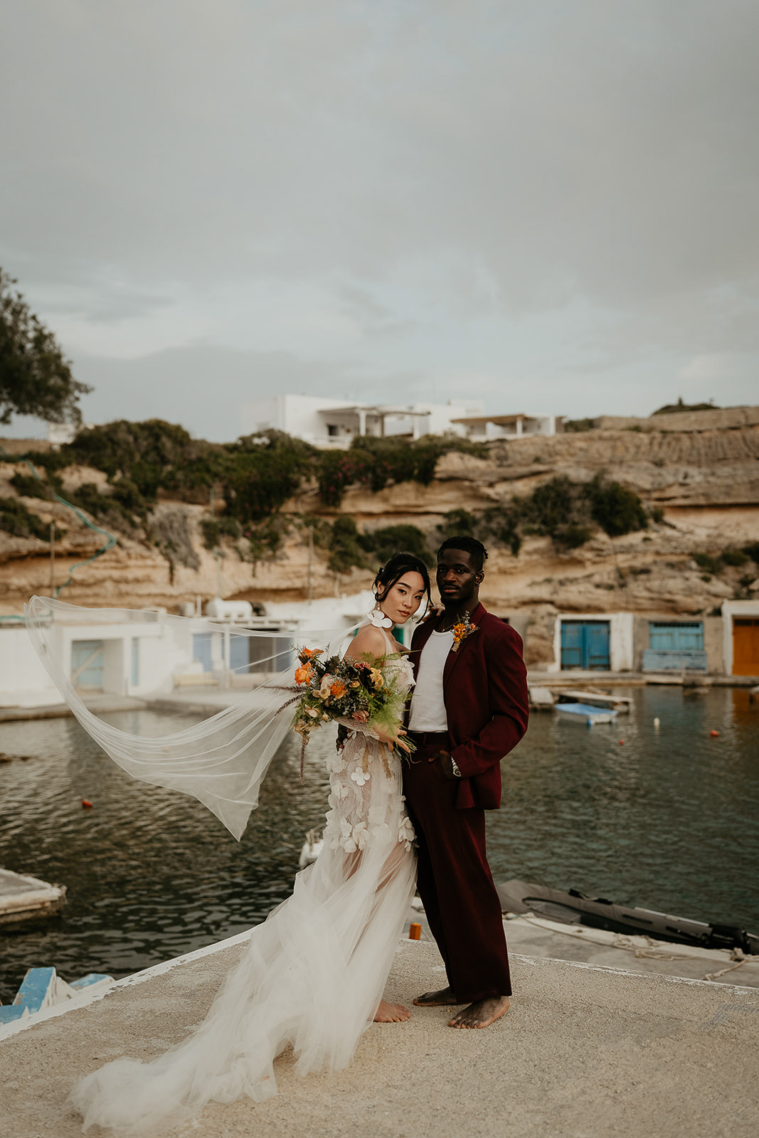 newlyweds posing in front of seaside buildings as they elope in Greece