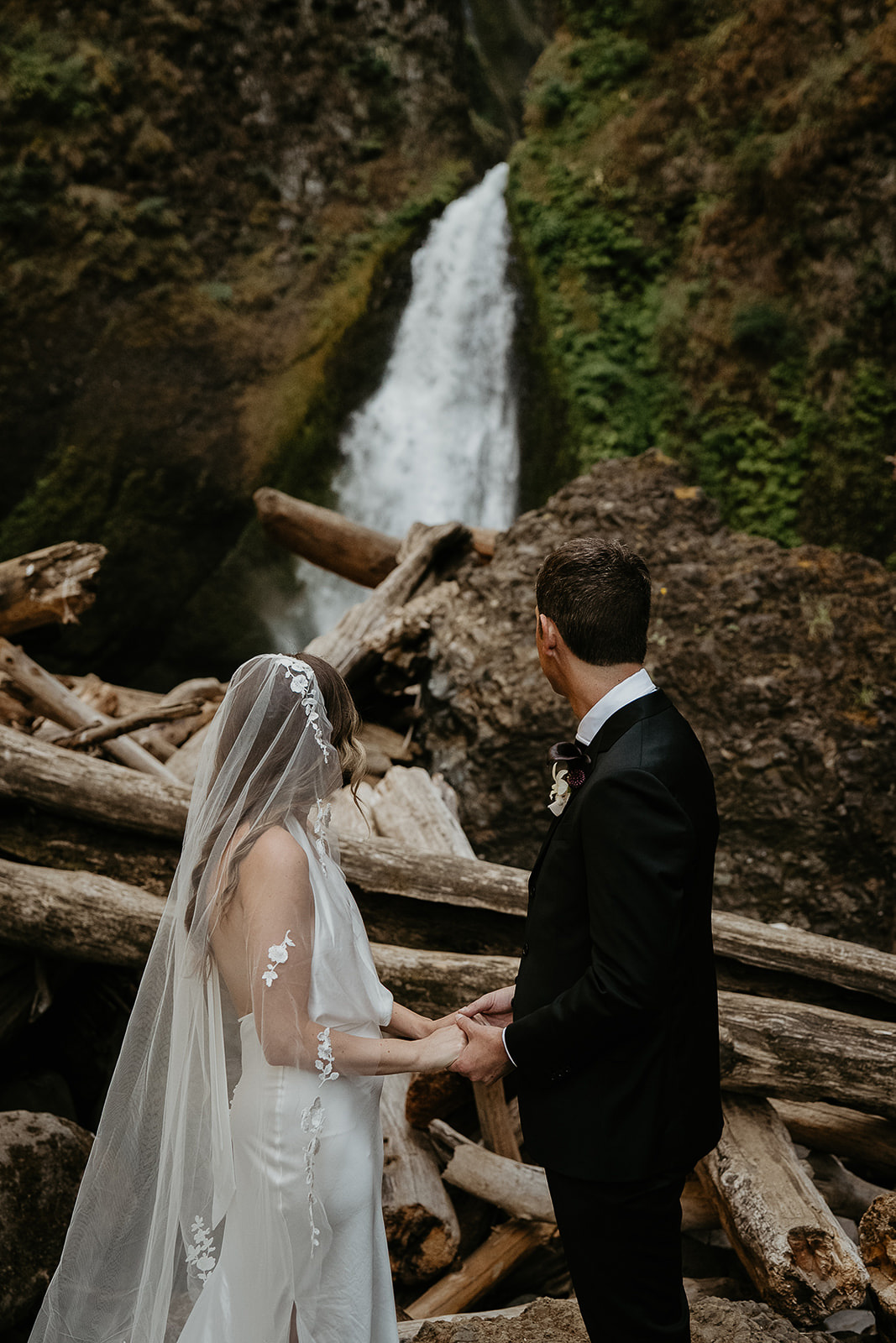 newlyweds holding hands in front of a waterfall during their elopement.