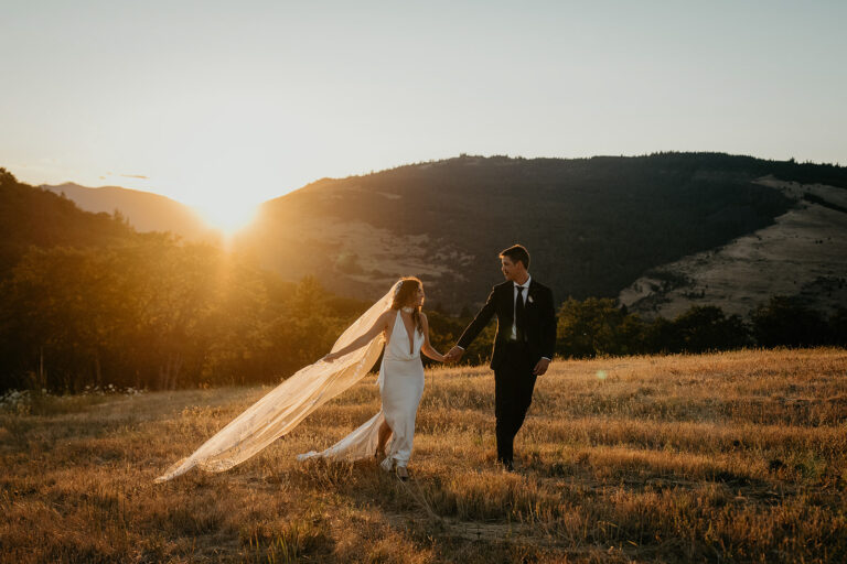 newlyweds holding hands frolicking through a field at sunset.