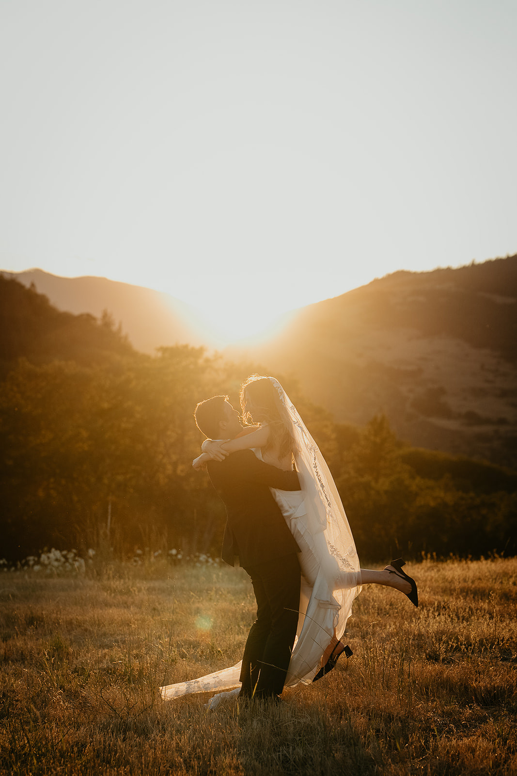 newlyweds hugging in a field at sunset.