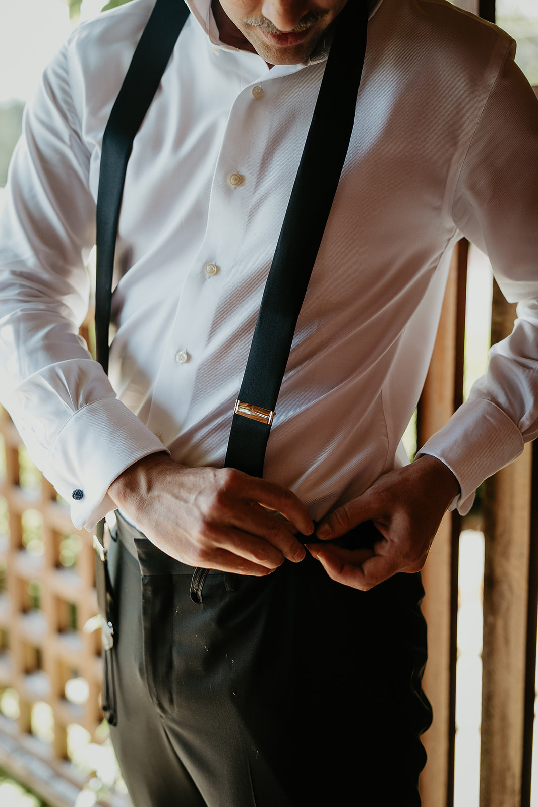 the groom adjusting his suspenders before his waterfall elopement.