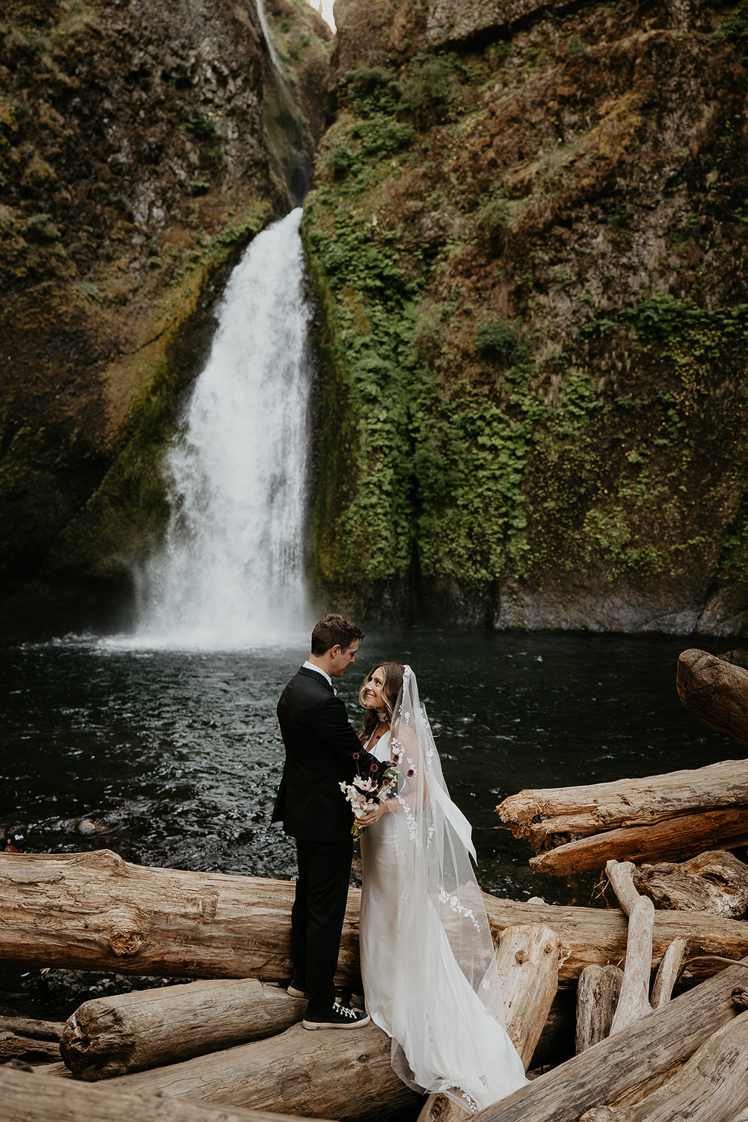 newlyweds kissing on a log by a waterfall during their elopement.