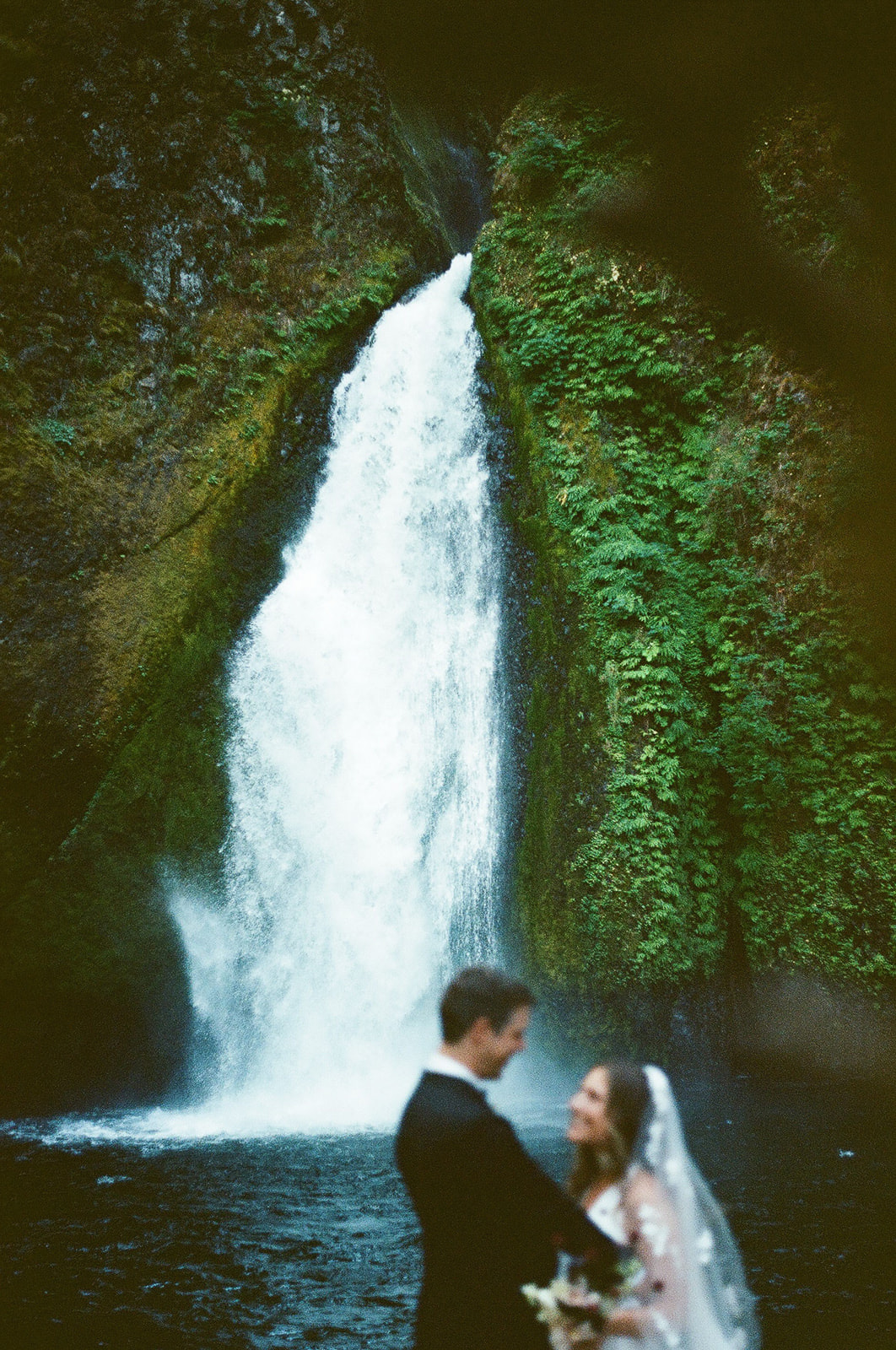 newlyweds smiling at each other with a waterfall in the background during their elopement.