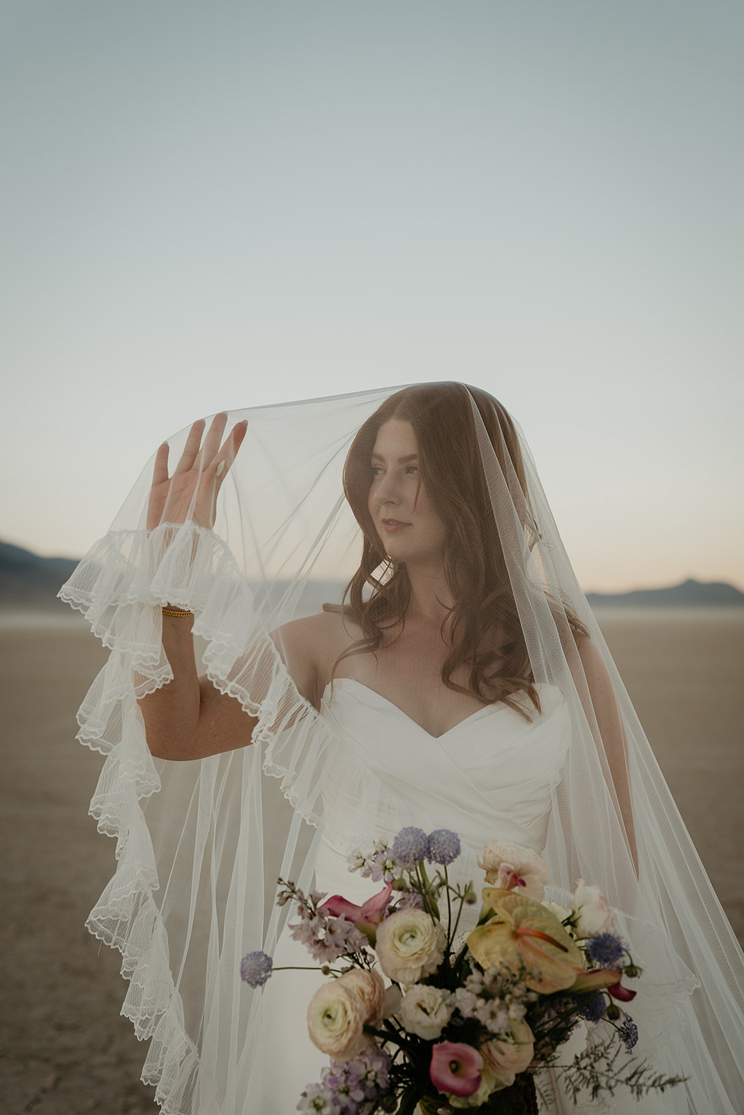 a bride holding her veil away from her face in the desert.
