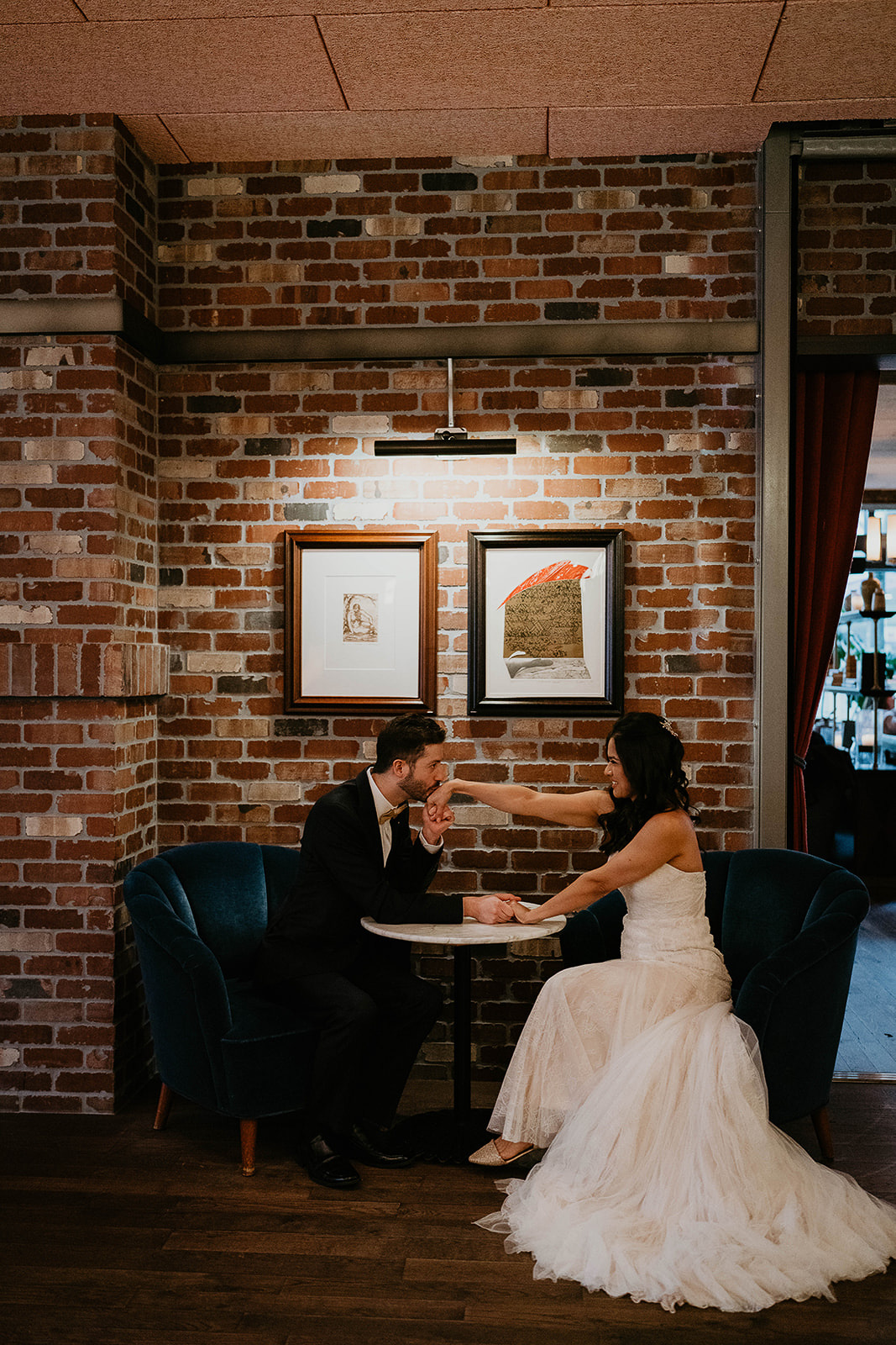 newlyweds holding hands on a table next to a brick wall.