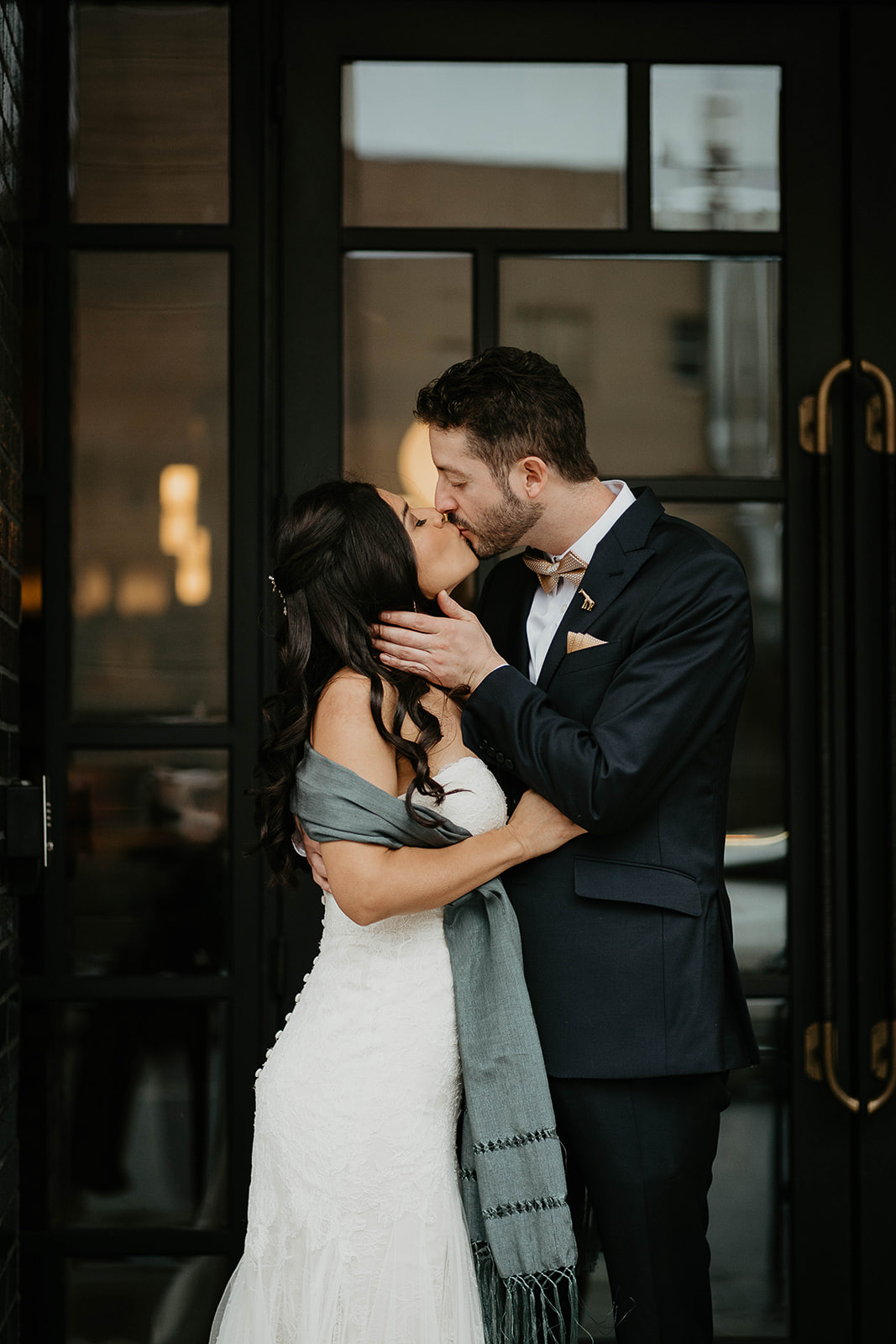 newlyweds kissing in front of a window framed by black beams.