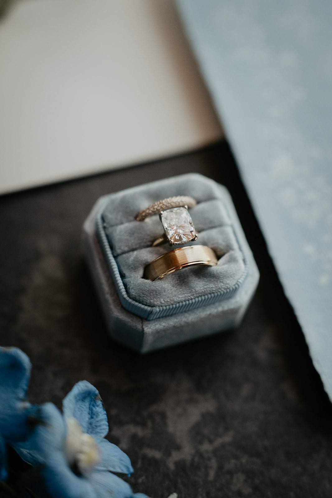 wedding rings in a ring box next to paper and flowers.